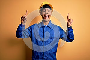 Young handsome african american worker man wearing blue uniform and security helmet smiling amazed and surprised and pointing up