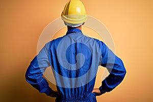 Young handsome african american worker man wearing blue uniform and security helmet standing backwards looking away with arms on