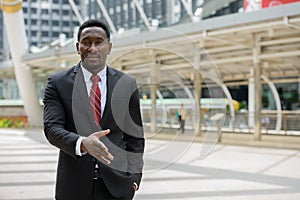 Young handsome African businessman giving handshake in the city outdoors