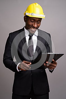 Young handsome African businessman with hardhat against gray bac