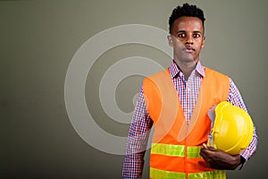 Young handsome African man construction worker against colored b