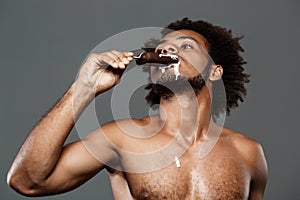 Young handsome african man eating icecream over grey background.