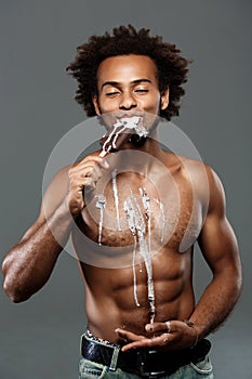 Young handsome african man eating icecream over grey background.