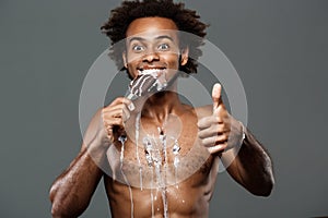 Young handsome african man eating icecream over grey background.