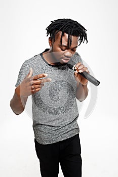 Young handsome african man singing in microphone over white background.