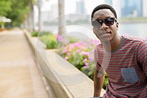 Young handsome African man wearing sunglasses and relaxing at the park