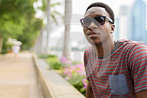 Young handsome African man wearing sunglasses and relaxing at the park