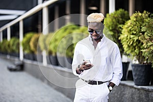 Young handsome Afro American man standing typing on cell phone outdoors in the summer street