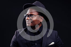 Young handsome afro american melancholy boy in a jacket and glasses on a black background in the studio.mystery and