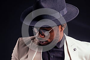 Young handsome afro american melancholy boy in a white jacket and glasses on a black background in the studio.mystery