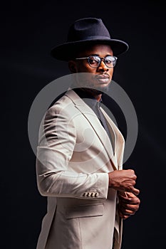 Young handsome afro american melancholy boy in a white jacket and glasses on a black background in the studio.mystery