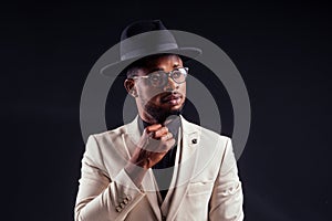 Young handsome afro american melancholy boy in a white jacket and glasses on a black background in the studio.mystery