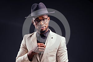 Young handsome afro american melancholy boy in a white jacket and glasses on a black background in the studio.mystery