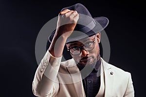 Young handsome afro american melancholy boy in a white jacket and glasses on a black background in the studio.mystery