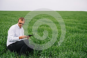 young handsome agronomist, agriculture engineer standing in green wheat field with tablet in hands in early summer