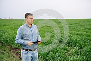 Young handsome agronomist, agriculture engineer standing in green wheat field with tablet in hands in early summer. Agribusiness