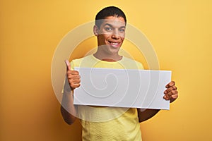 Young handsome arab man holding banner standing over isolated yellow background happy with big smile doing ok sign, thumb up with