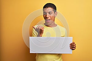 Young handsome arab man holding banner standing over isolated yellow background pointing and showing with thumb up to the side