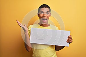 Young handsome arab man holding banner standing over isolated yellow background very happy and excited, winner expression