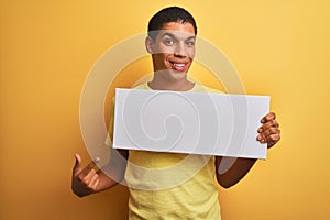 Young handsome arab man holding banner standing over isolated yellow background very happy pointing with hand and finger