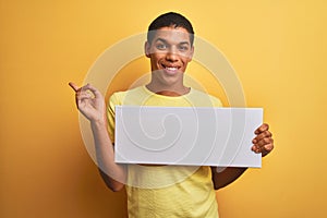 Young handsome arab man holding banner standing over isolated yellow background very happy pointing with hand and finger to the