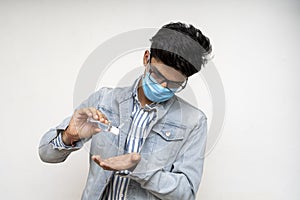 Young handsome asian boy in denims wearing a mask using a hand sanitizer