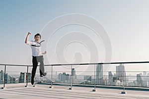 Young handsome Asian businessman jumping celebrate success winning pose on building roof. Work, job, or success concept