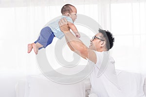 Young handsome Asian father happily playing with his 5 months baby boys. Healthy newborn baby boys with father in bed room