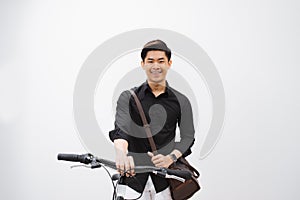 Young handsome asian man against the backdrop of white wall sits on a bicycle