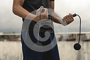 A young handsome asian man holding a cordless jumping ropes outside a floor deck. Cardio training exercise regimen