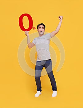 Young handsome Asian man holding up to 0% and happy celebrating on yellow background for no interest installment payment concept photo