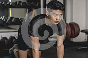 A young handsome asian man mentally prepares before starting a set of Bird-Dogs on a mat at the gym. Doing simple core exercises