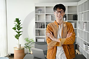 Young handsome Asian man standing with arms crossed in the office room with confident