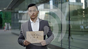 A young handsome Asian man in a suit standing on the street with a sign - Looking for a job.