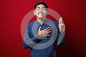 Young handsome asian man wearing casual shirt smiling swearing with hand on chest and fingers up, making a loyalty promise oath