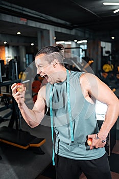 young handsome athlete hungry and eating healthy apple fruit in gym