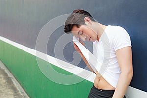 Young handsome athlete man wiping sweat on his face with his white T-shirt on sport club background after exercise