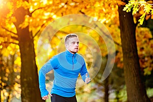 Young handsome athlete running outside in sunny autumn nature