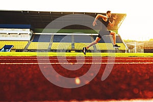 Young handsome athlete running at the stadium at sunset
