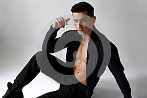 Young handsome athletic man posing in studio, wearing in black clothes, sit down,  on white background.