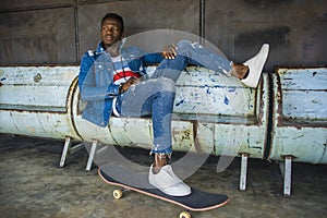 Young handsome and attractive black African American skateboarder man sitting on city grunge bench holding skate board posing in