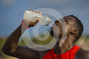 Young handsome and attractive black African American sport man tired and thirsty after running workout holding bottle drinking