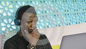 Young handsome and attractive black afro American man working with laptop computer and headphones concentrated and thoughtful in