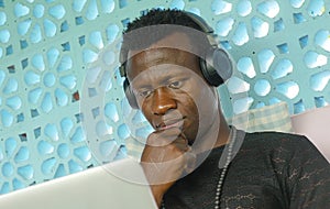 Young handsome and attractive black afro American man working with laptop computer and headphones concentrated and thoughtful in