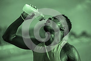 Young handsome and attractive black afro American sport man tired and thirsty after running workout holding bottle drinking water