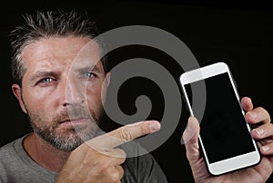 Young handsome and attractive Caucasian man holding mobile phone in his hand pointing it with the finger isolated on black