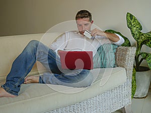 Young handsome and attractive happy man doing internet shopping thoughtful online with credit card sitting relaxed at home sofa co