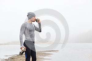 Young handsome attractive man at lake, posing with beautiful foggy river on background, side view of pensive man enjoying hot