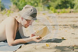 Young handsome attractive man in panama lying on sandy heaven beach and reading a book on a summer day