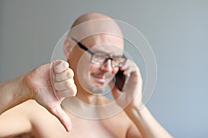 Young handsome bald man in black glasses talking on the phone. Closeup portrait of a man. Bad news, sadness. A man shows his thumb